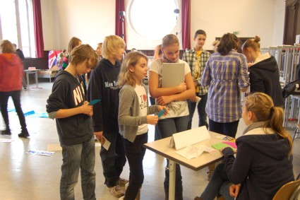 Mädchengruppe vor einem Tisch, hinter dem eine Schülerin sitzt